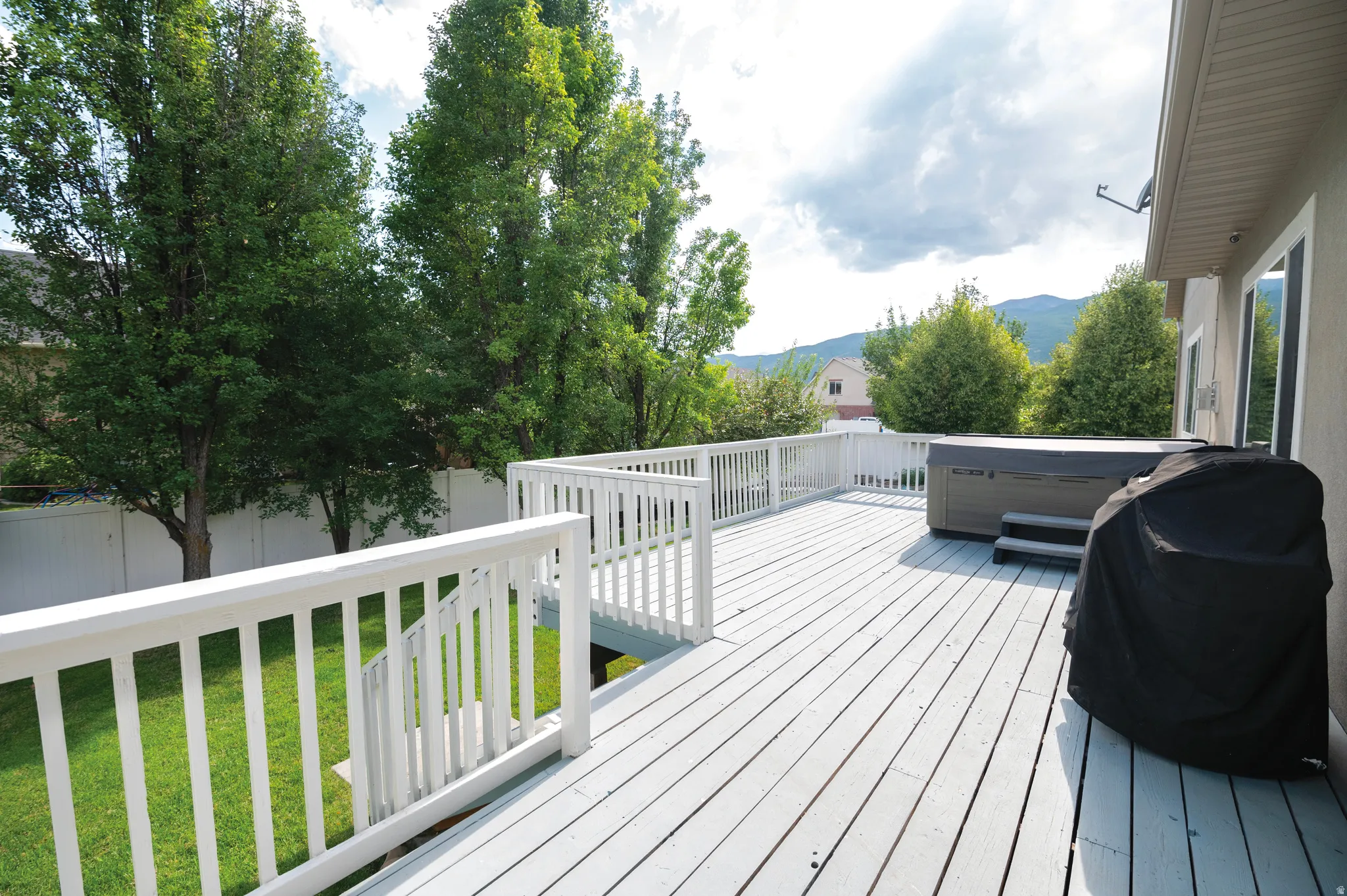 Deck featuring a grill, a fenced backyard, a mountain view, and a hot tub