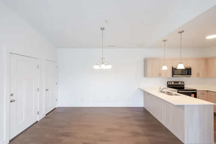 Open-concept living space featuring wood-finish flooring, a contemporary kitchen, light wood cabinetry, a built-in microwave, and a breakfast bar with dual pendant lighting