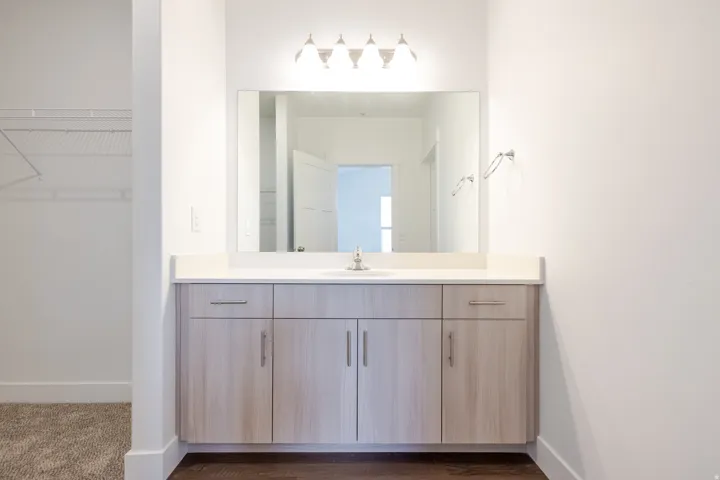 Bathroom vanity featuring a light wood-finish cabinet with brushed nickel hardware, a white countertop, and an undermount sink