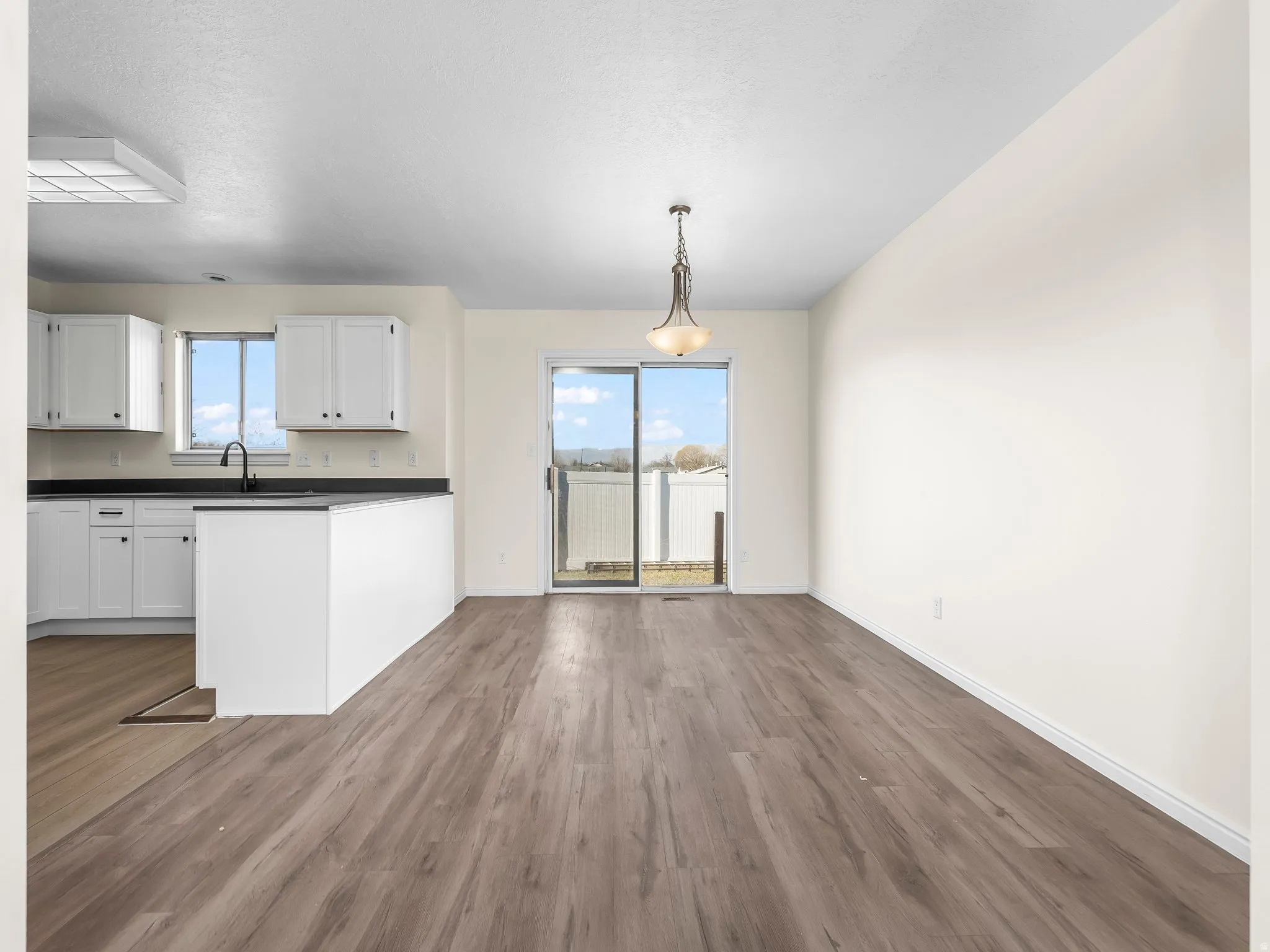 Kitchen featuring dark countertops, white cabinetry, pendant lighting, dark wood-style flooring, and a peninsula