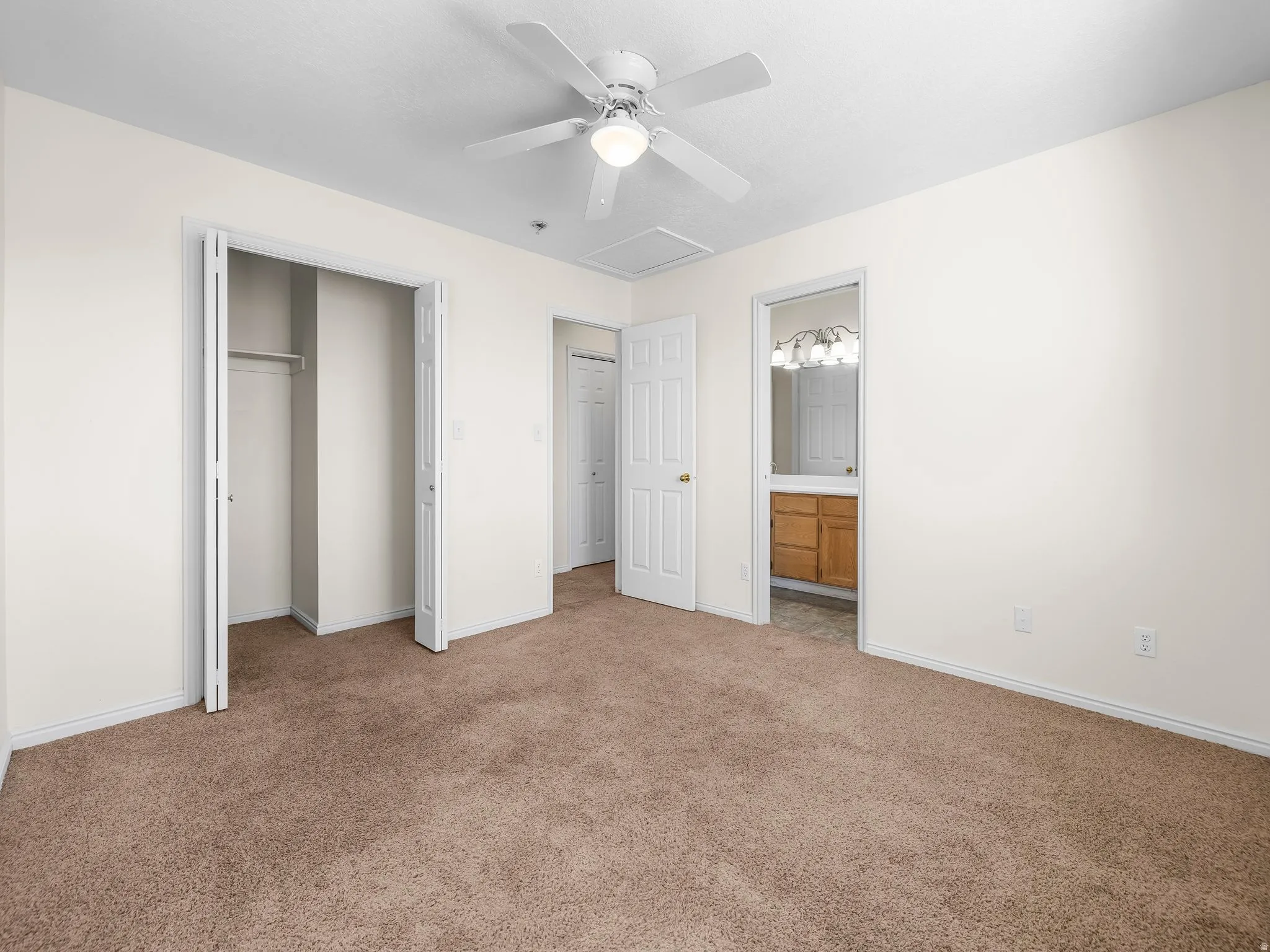 Unfurnished bedroom featuring carpet flooring, a closet, ceiling fan, attic access, and ensuite bathroom