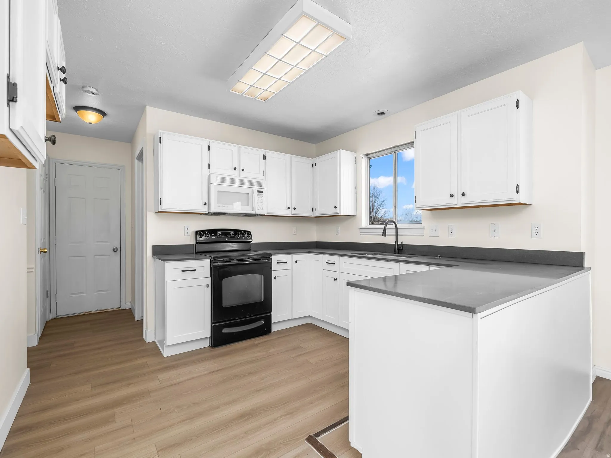 Kitchen featuring electric range, white cabinetry, light wood-style flooring, white microwave, and a peninsula
