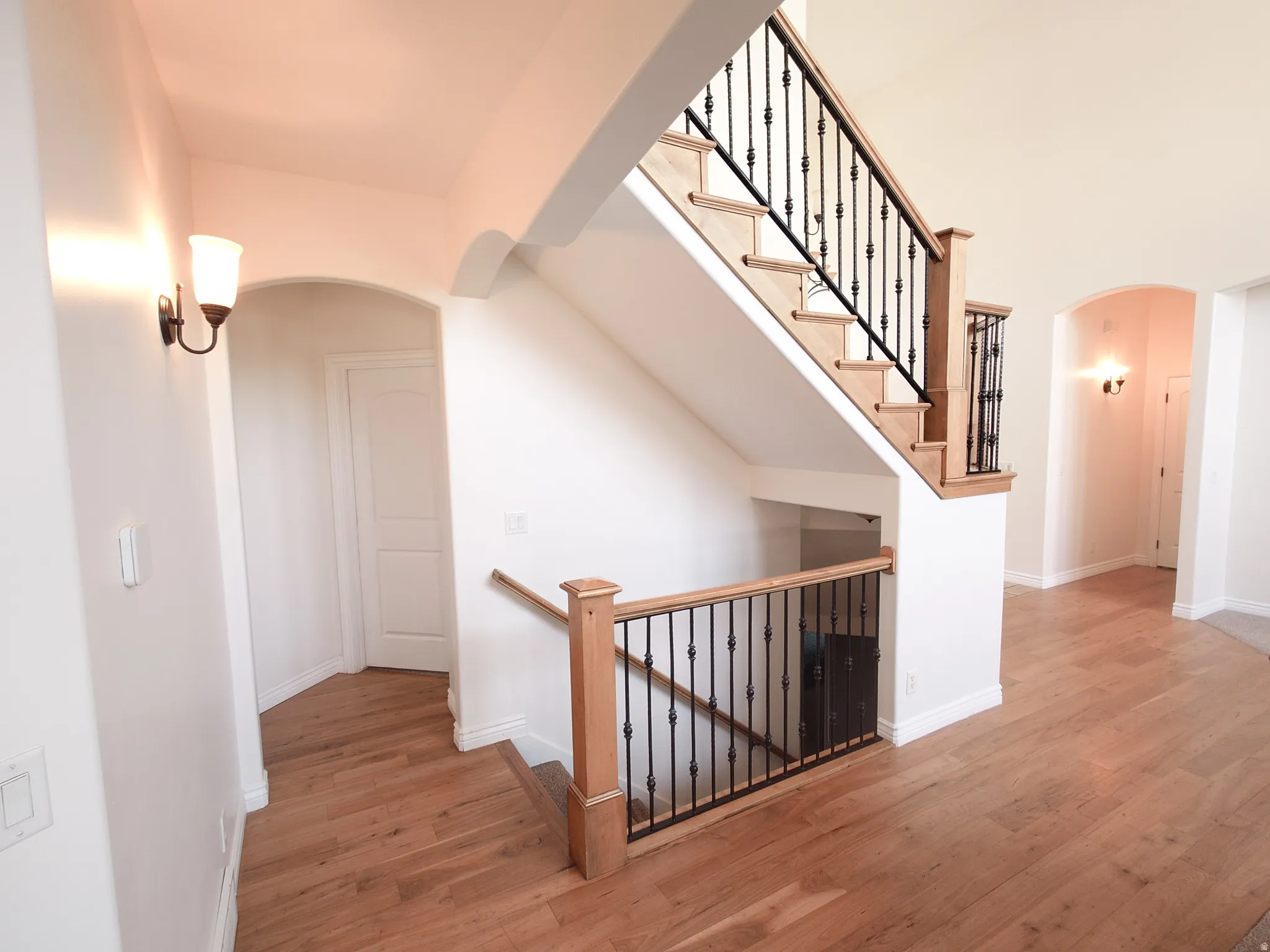 Hallway with arched walkways, light wood-type flooring, and an upstairs landing
