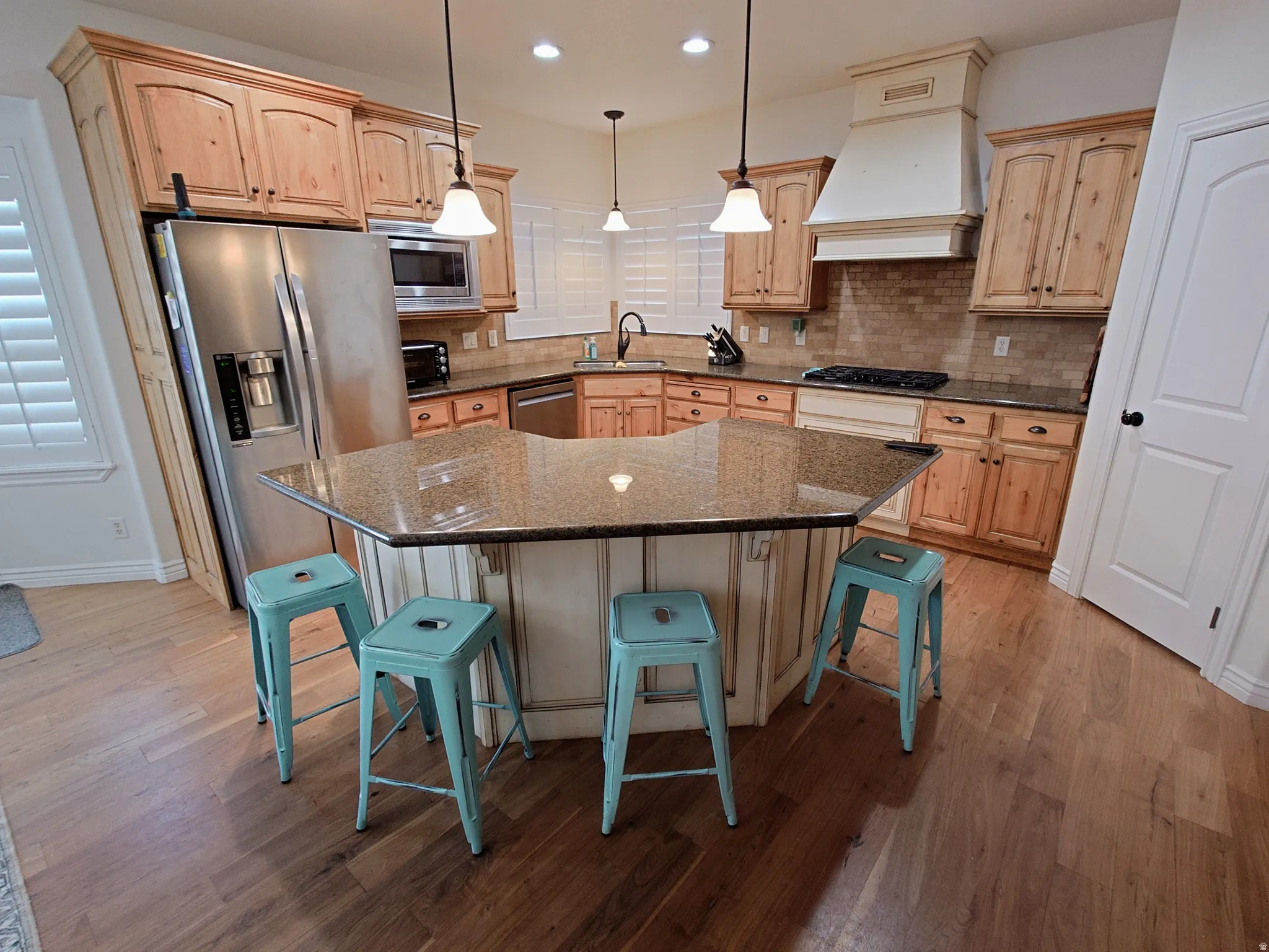 Kitchen featuring a kitchen bar, pendant lighting, appliances with stainless steel finishes, a center island, and light brown cabinets