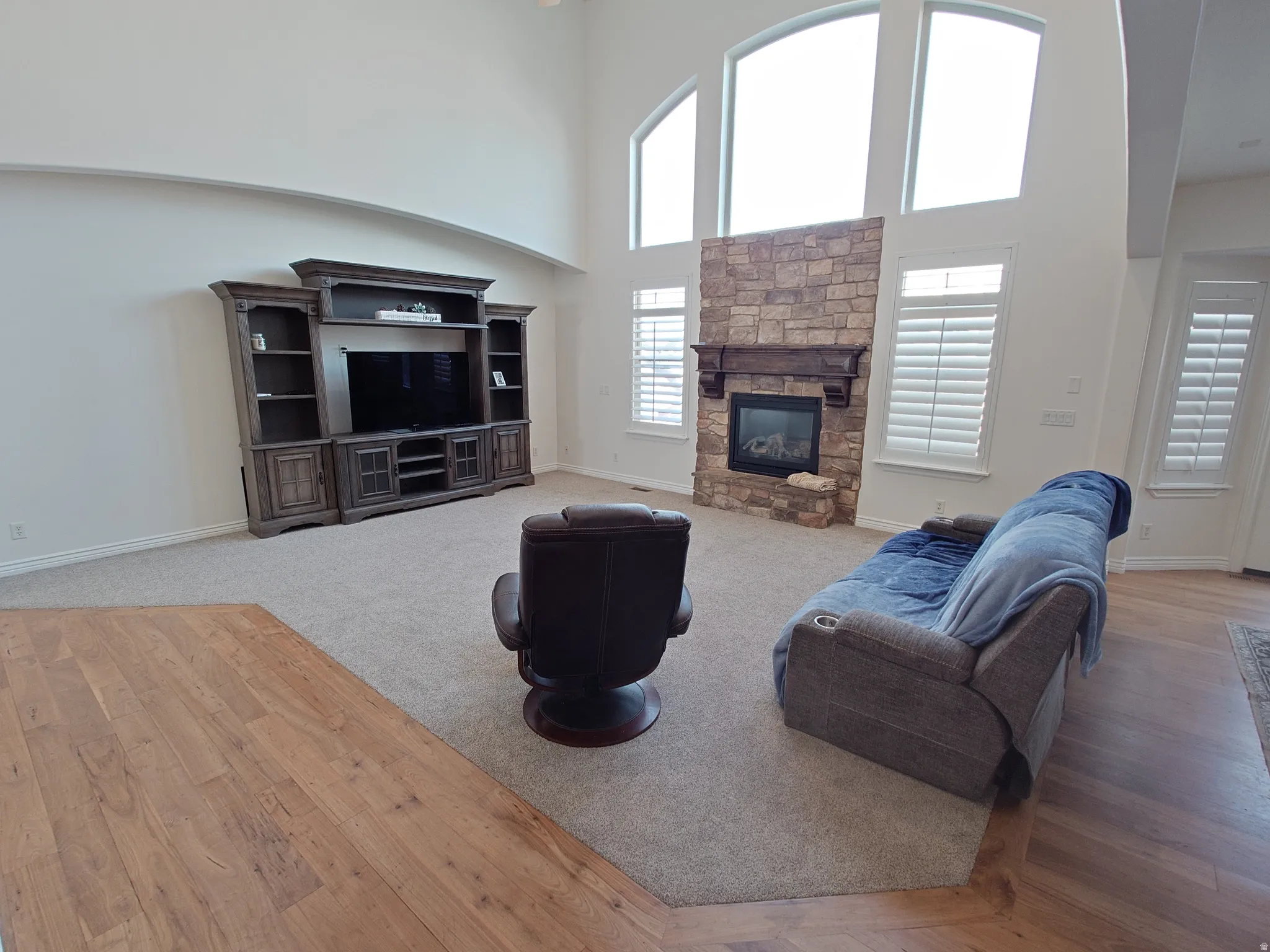 Living room featuring a high ceiling, a stone fireplace, and light wood finished floors