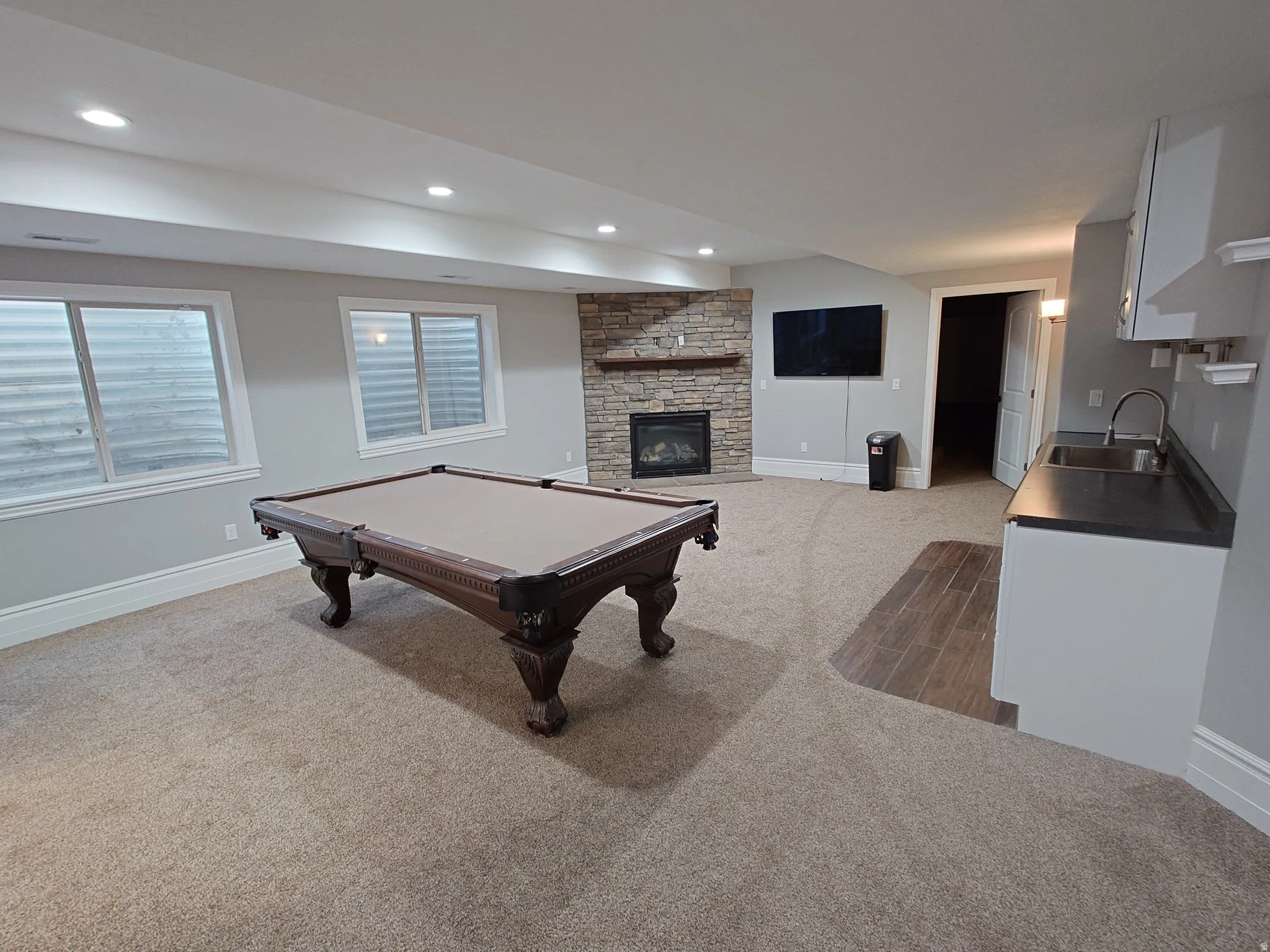 Game room with a stone fireplace, billiards, and light carpet