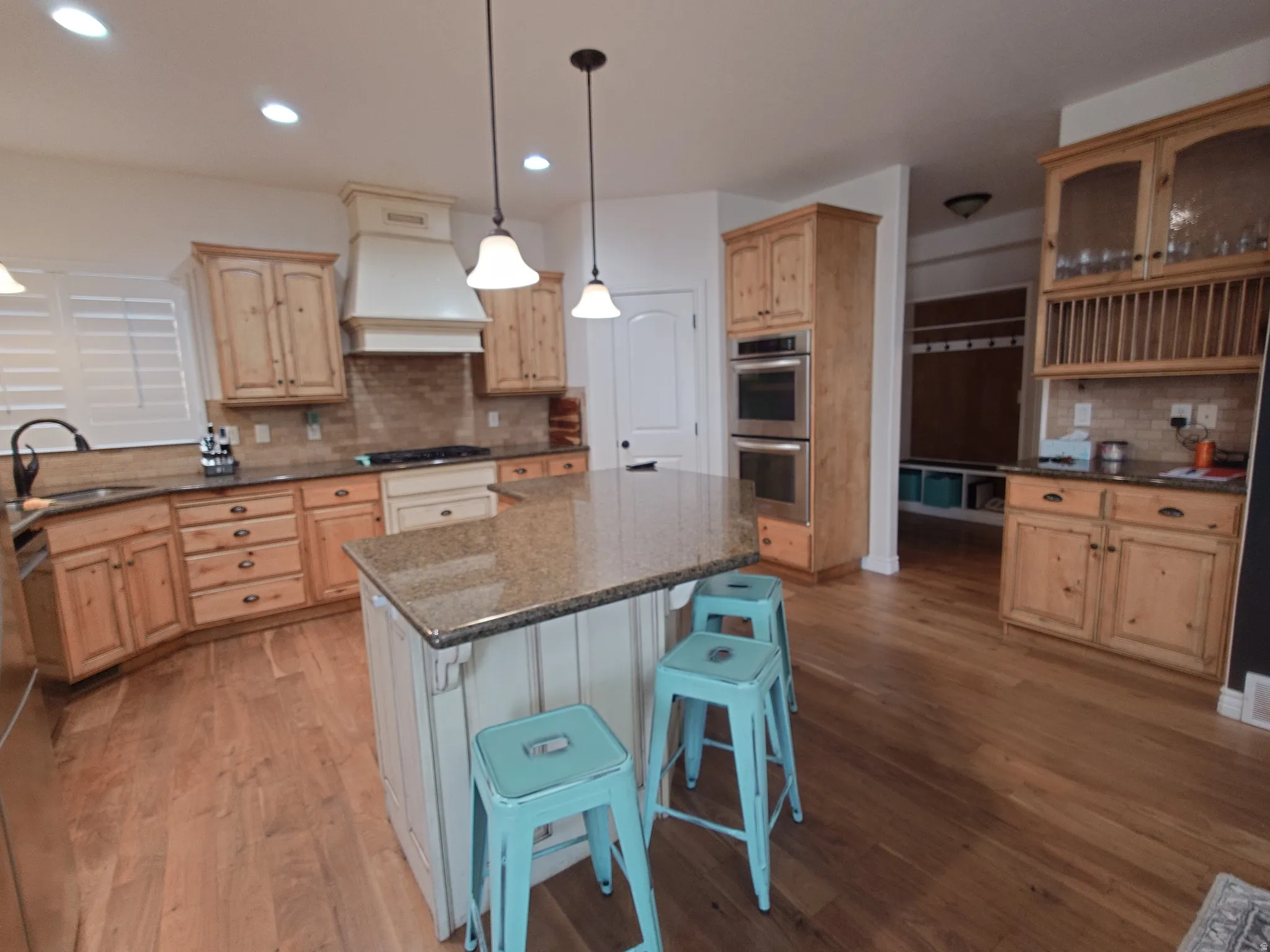 Kitchen with decorative light fixtures, backsplash, dark stone counters, custom range hood, and recessed lighting
