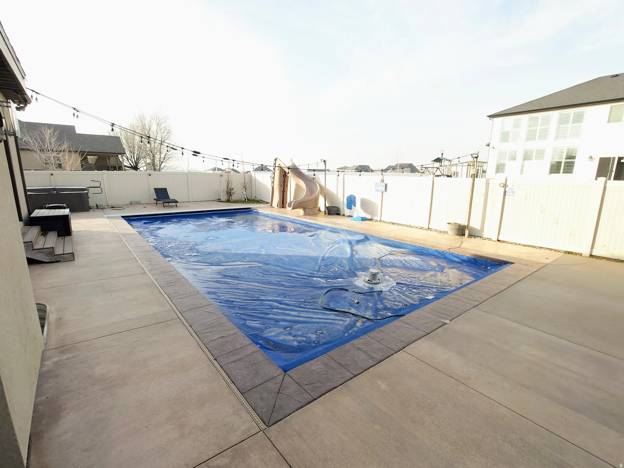 View of swimming pool with a water slide, a fenced backyard, and a patio