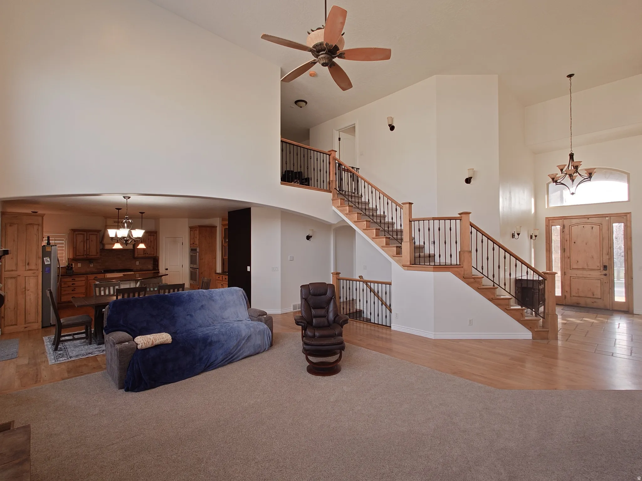 Living area with a chandelier, a towering ceiling, light wood-type flooring, stairway, and light colored carpet