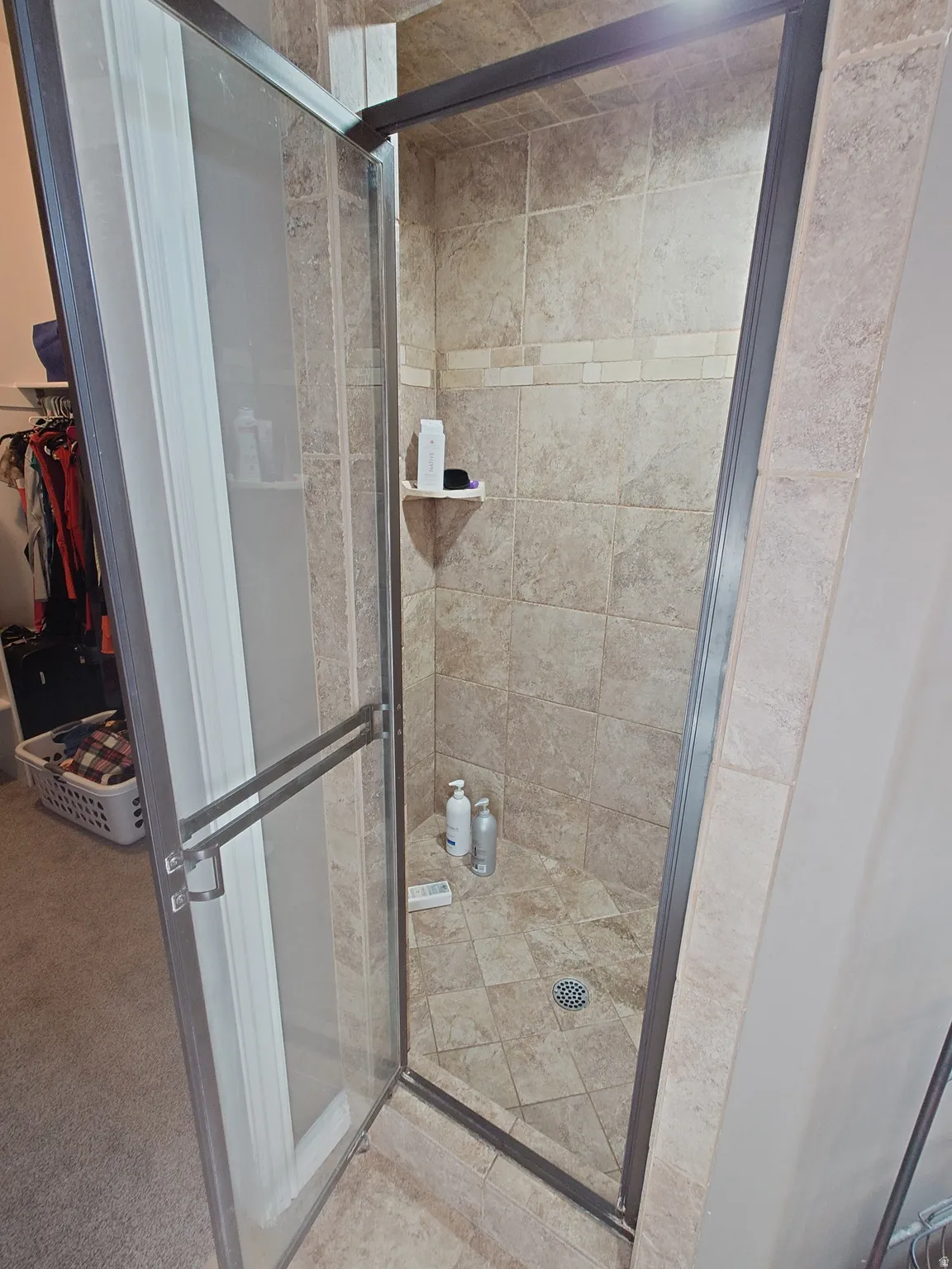 Full bath with a shower stall, a walk in closet, and light carpet
