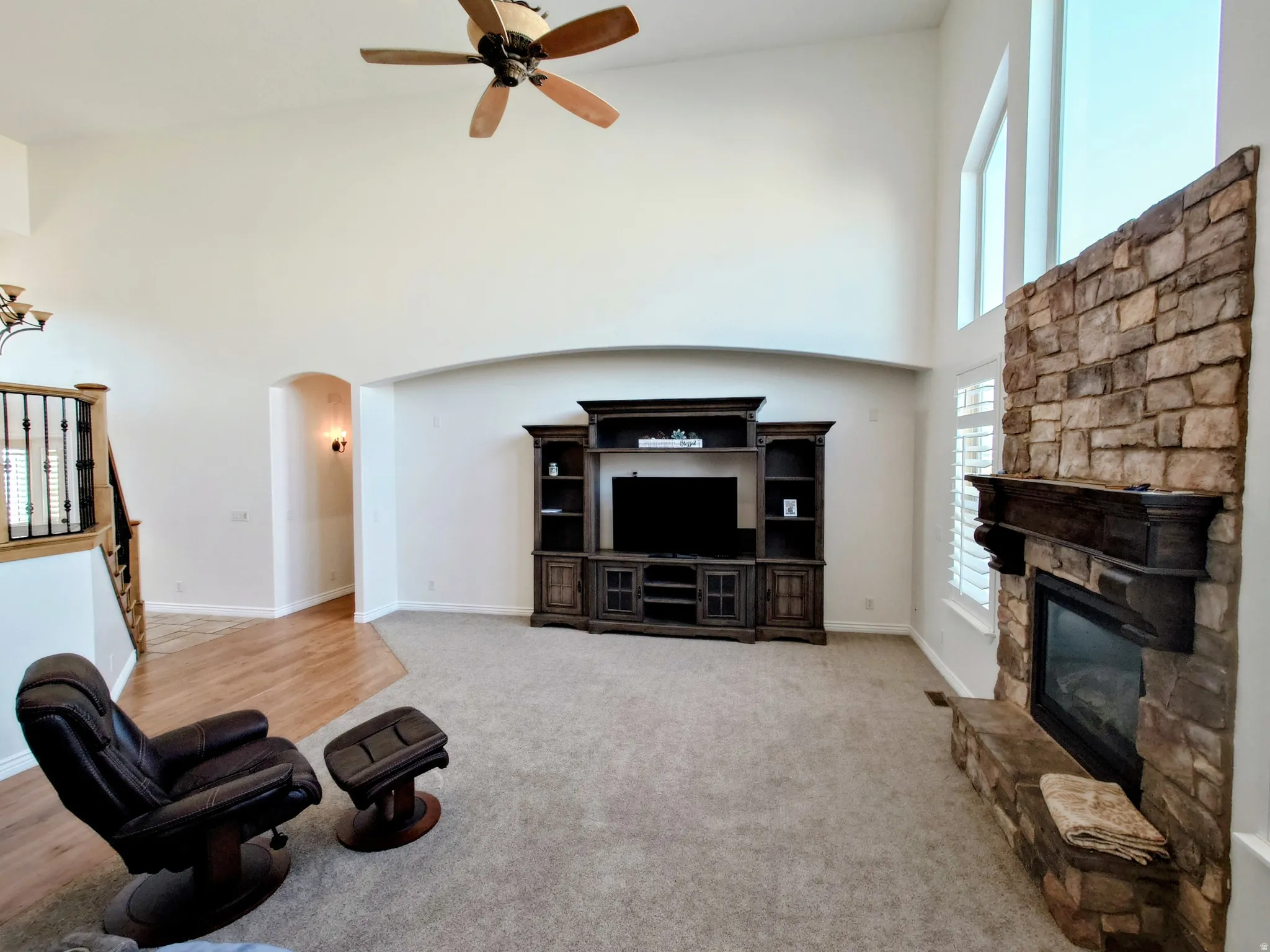 Living area with a towering ceiling, a fireplace, arched walkways, ceiling fan, and light carpet