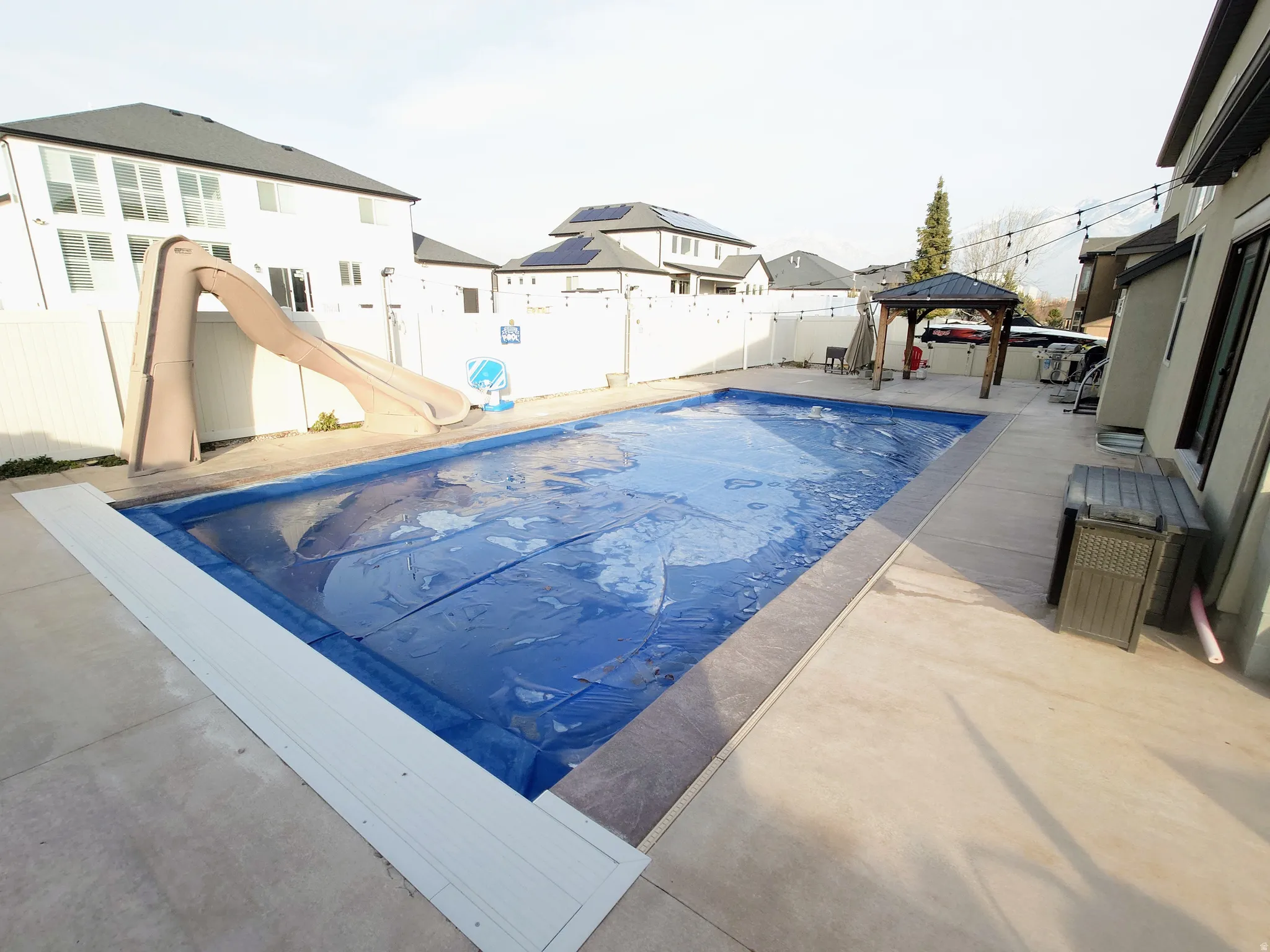 View of pool featuring a gazebo, a water slide, a patio area, and a fenced backyard