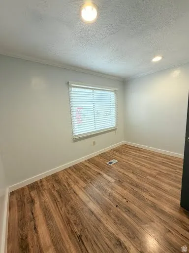 Unfurnished room with dark wood-style floors, a textured ceiling, and ornamental molding