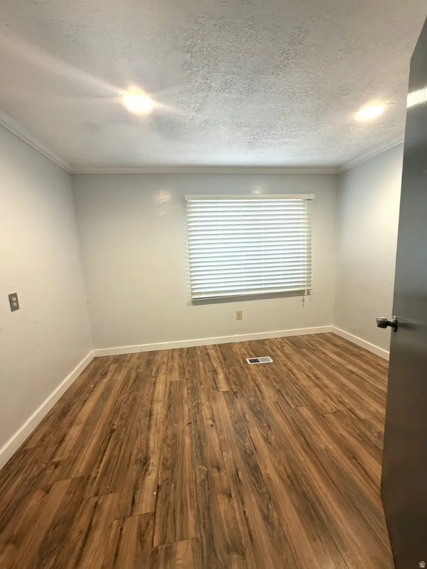 Unfurnished room with dark wood finished floors, a textured ceiling, and crown molding
