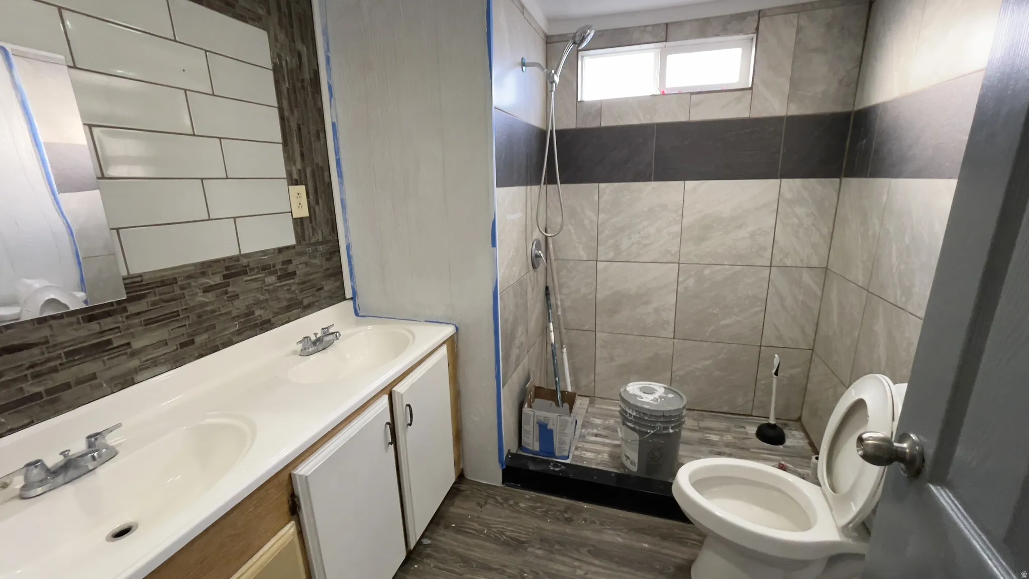 Full bathroom featuring a stall shower, double vanity, backsplash, and dark wood-style flooring