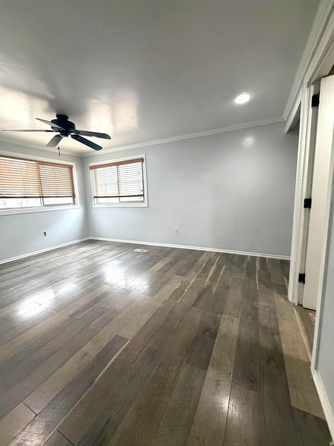 Empty room featuring dark wood-type flooring, ceiling fan, and crown molding
