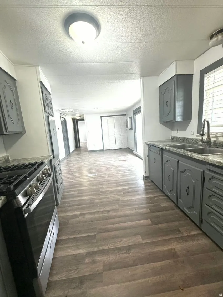Kitchen featuring gray cabinetry, stainless steel gas range, a textured ceiling, open floor plan, and dark wood-type flooring