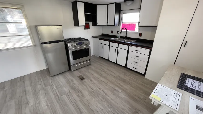Kitchen with stainless steel appliances, dark countertops, white cabinetry, light wood-style floors, and open shelves