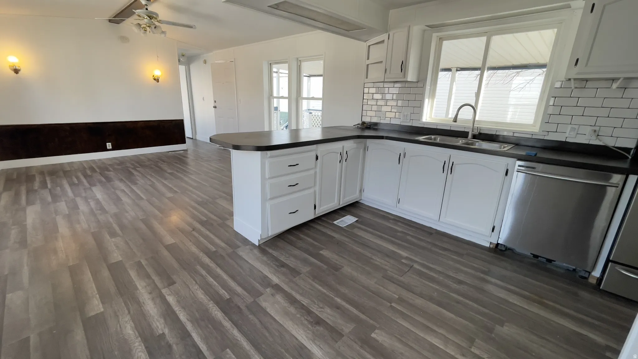 Kitchen featuring a peninsula, open floor plan, white cabinetry, dark countertops, and lofted ceiling
