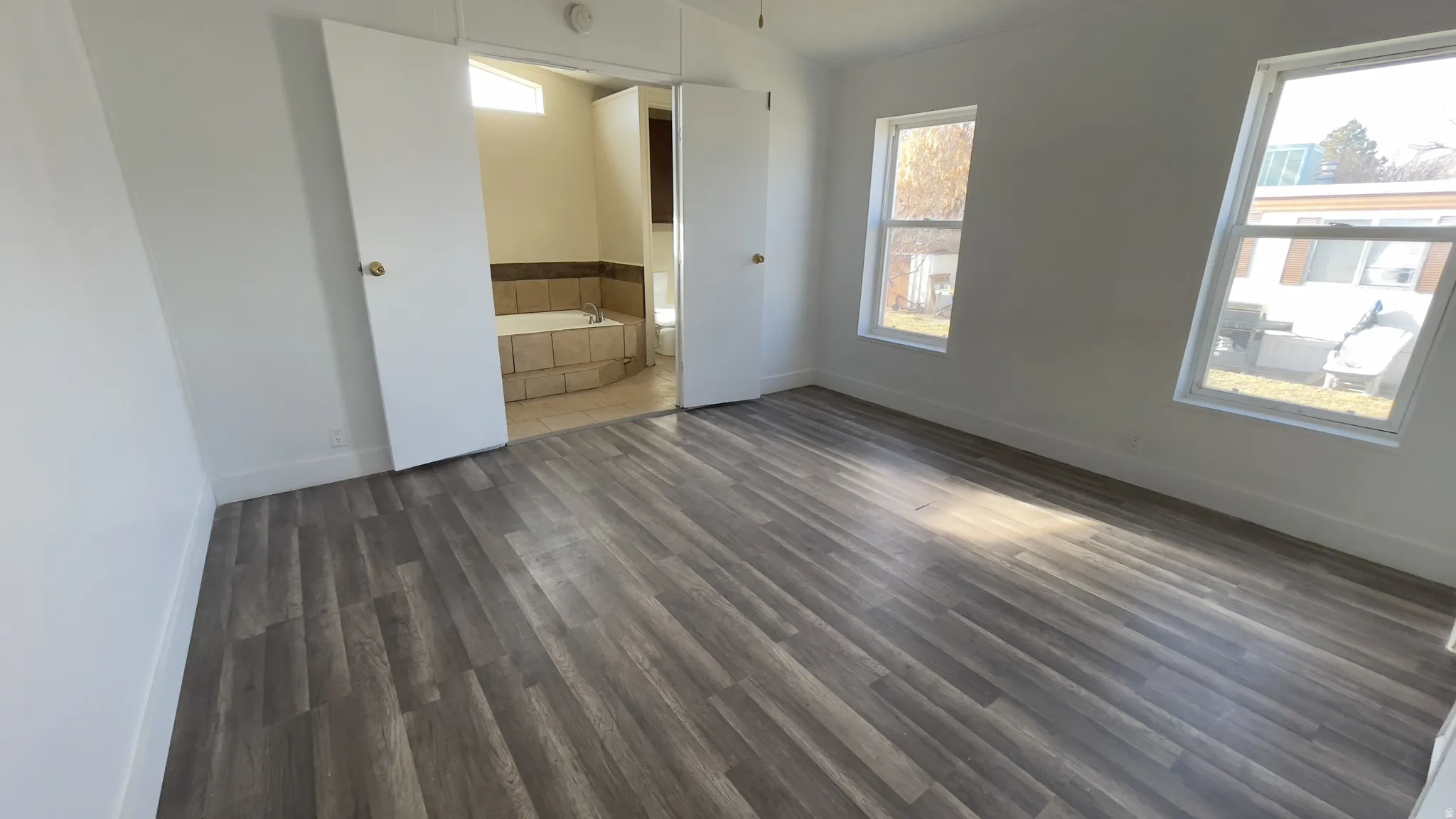 Unfurnished bedroom with dark wood-style flooring, lofted ceiling, and connected bathroom