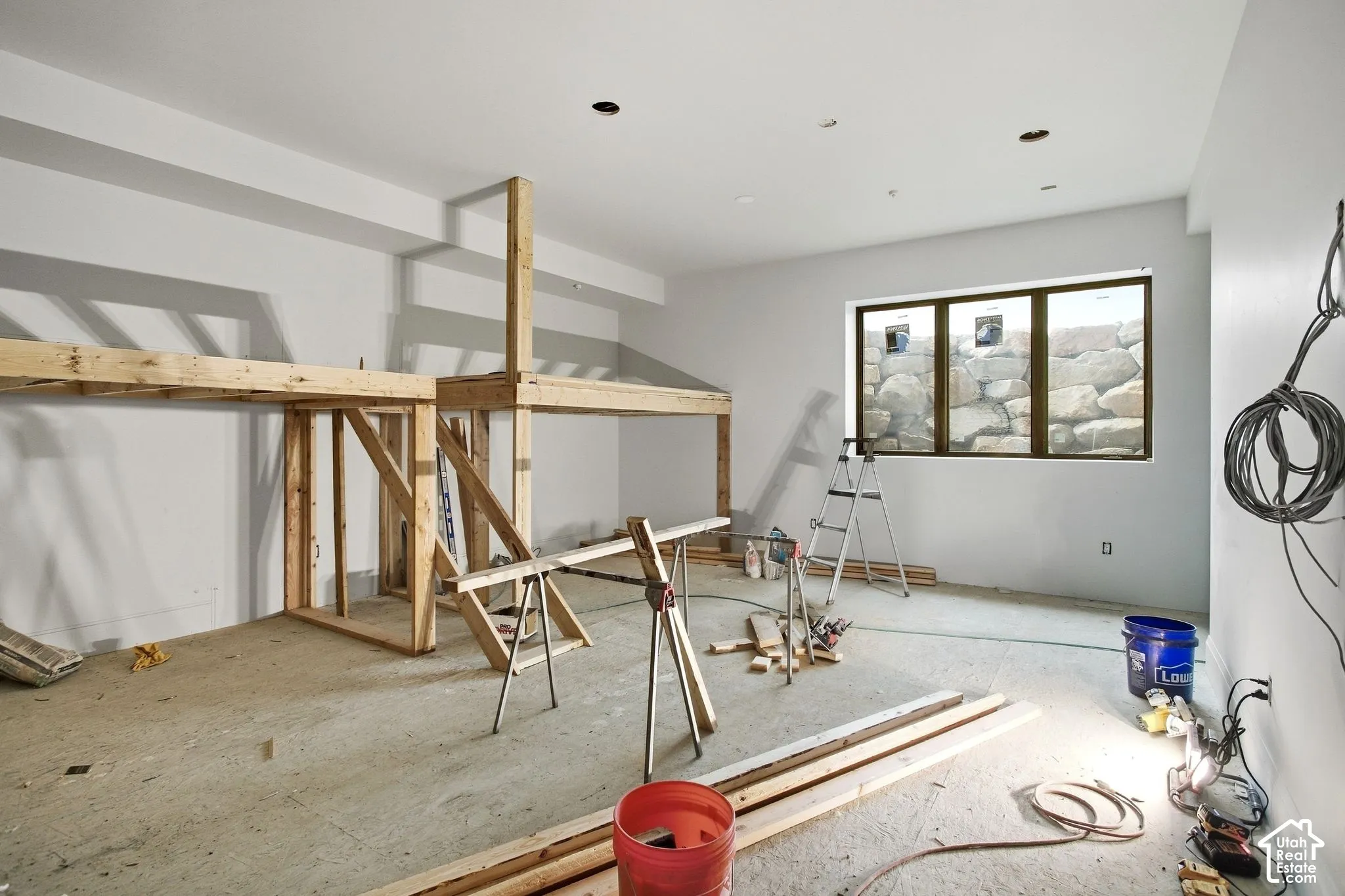 Unfinished interior space featuring a partial wood-frame structure, a three-panel window, and concrete flooring