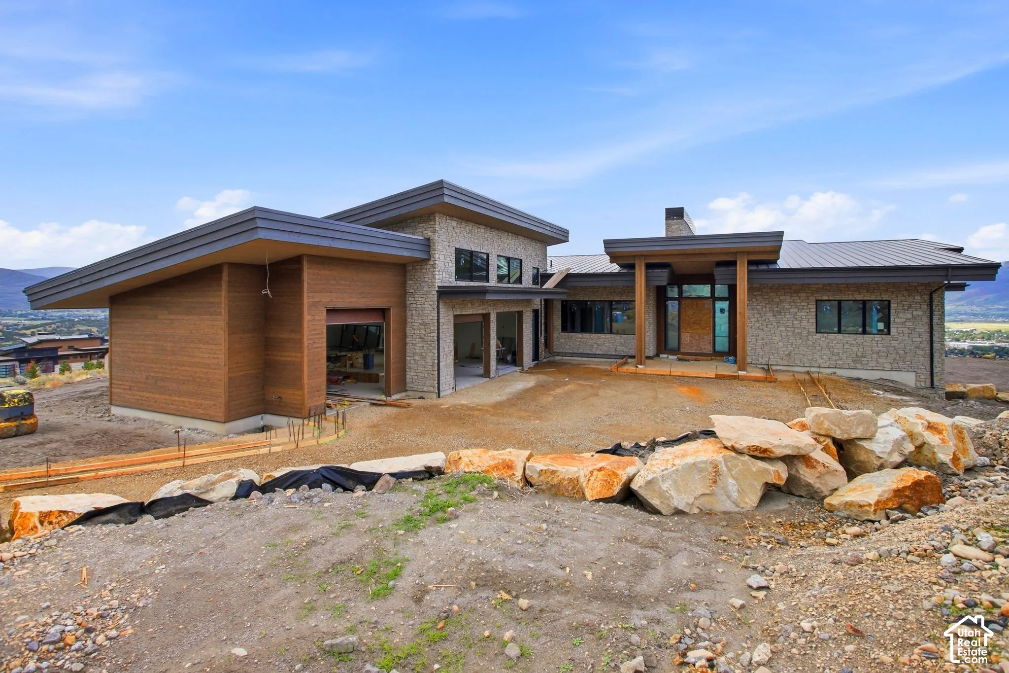 Contemporary exterior featuring wood siding, stone veneer accents, an angular roofline, and an integrated garage