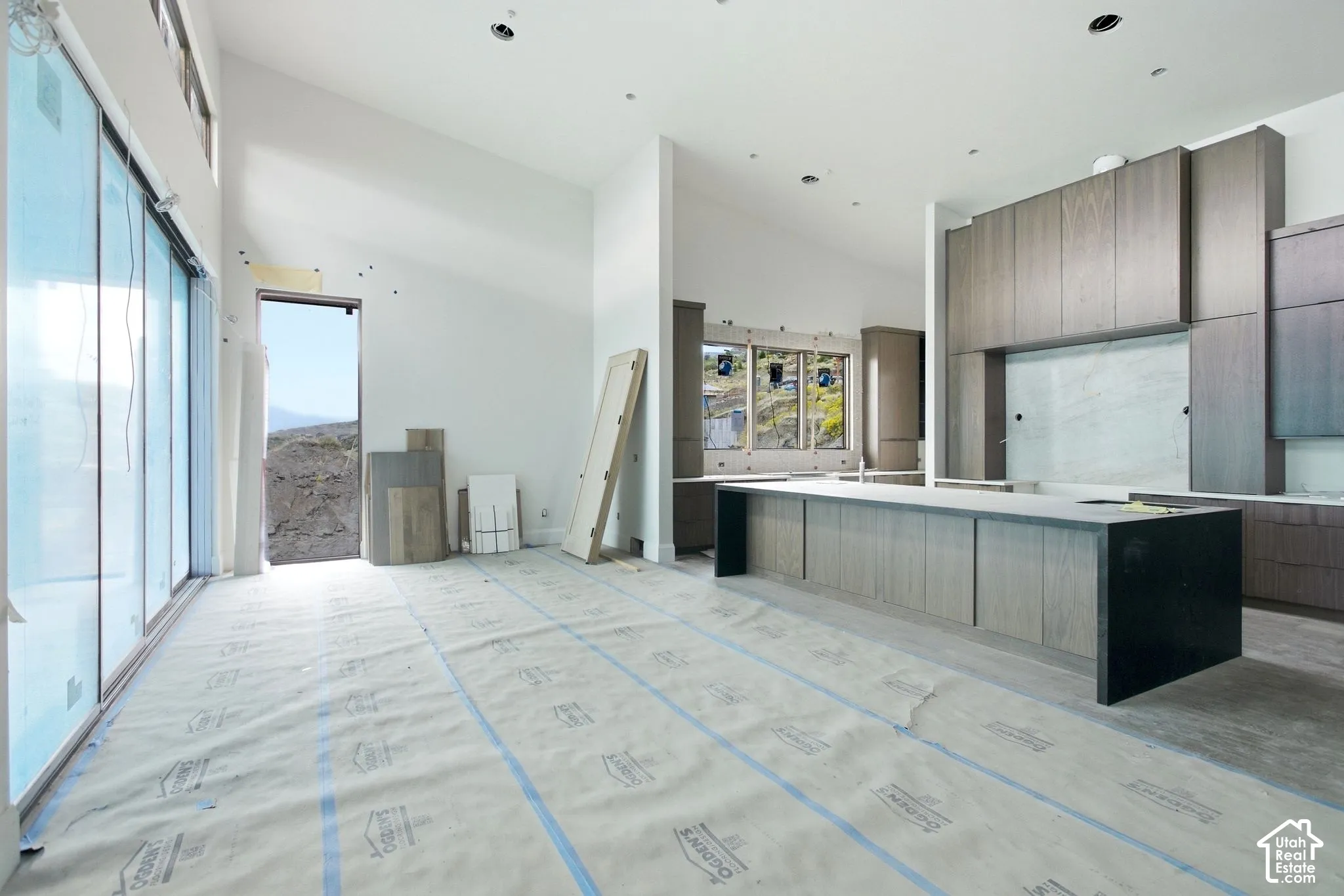 Vaulted ceilings, expansive sliding glass doors, contemporary kitchen cabinetry, large kitchen island with dark finish accent, and recessed lighting