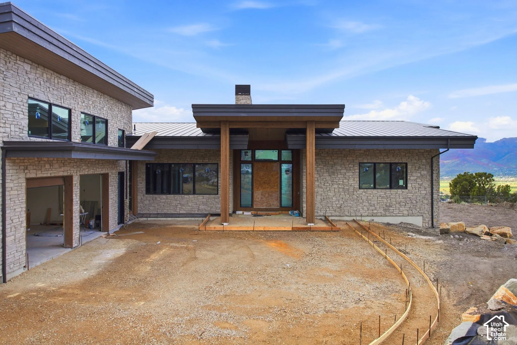 Contemporary exterior featuring stone veneer siding, dark-framed windows, a prominent covered entry with wood structural columns, and a metal roof