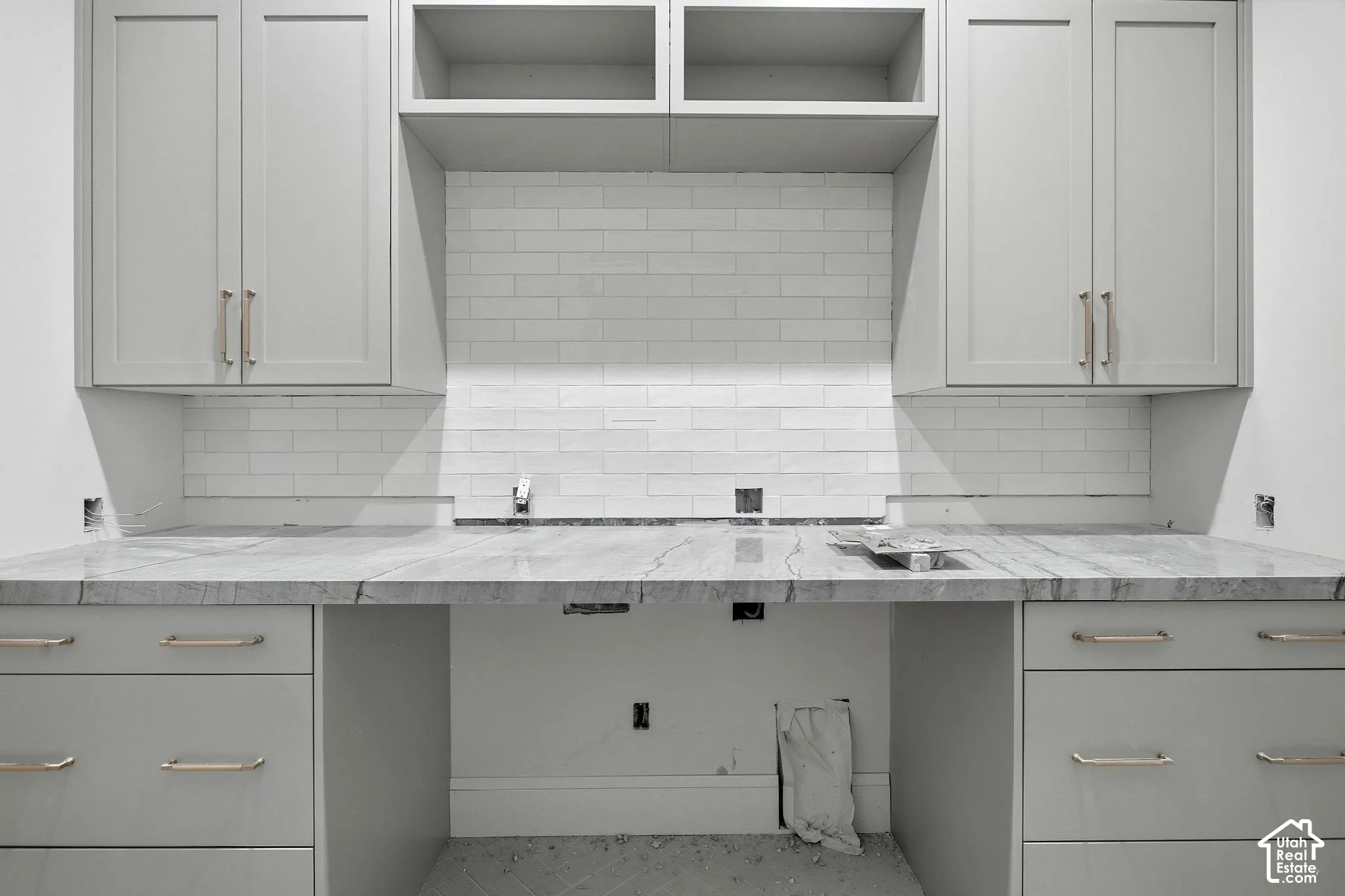 Light gray cabinetry with brushed nickel hardware, marble-finish countertops, subway tile backsplash, and open shelving