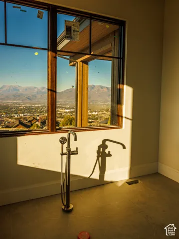 Floor-mounted tub filler with a handheld shower attachment, large picture window with dark-toned framing, and mountain scenery
