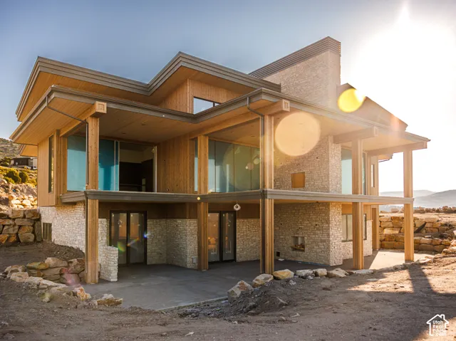 Multi-level architectural exterior featuring natural stone masonry, vertical wood siding, expansive glass windows, and a covered lower-level patio