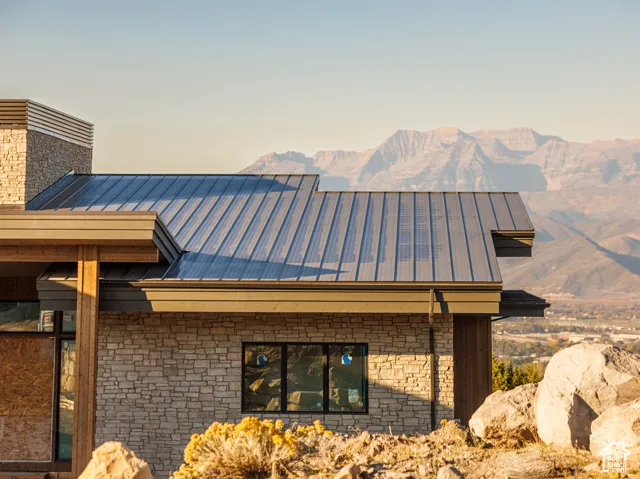 Exterior architectural detail featuring stacked stone siding, metal roofing, prominent wood beams, and mountain scenery