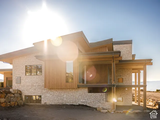 Contemporary exterior featuring stacked stone masonry, horizontal wood-finish siding, multi-level shed rooflines, and a covered patio supported by structural posts