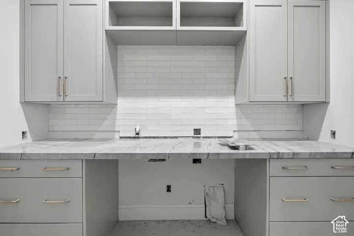 Light gray cabinetry with brushed nickel hardware, marble-finish countertops, subway tile backsplash, and open shelving