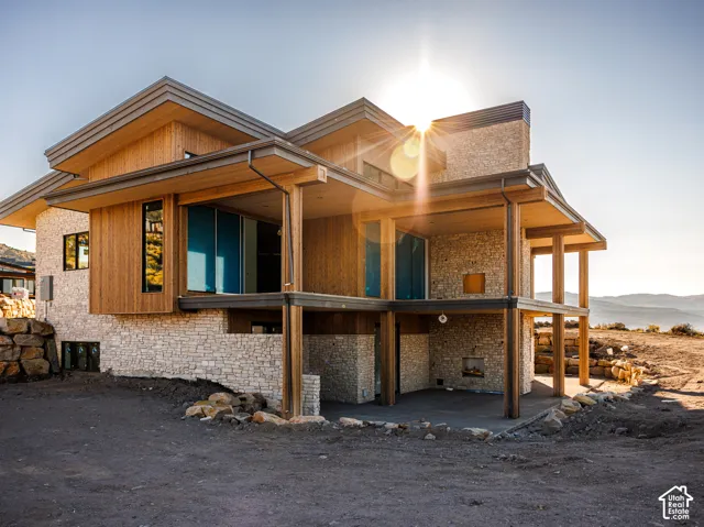 Contemporary two-story exterior featuring stone veneer masonry, vertical wood-finish siding, a multi-level covered deck, and a built-in outdoor fireplace