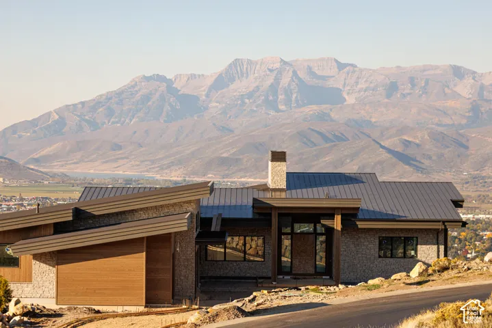 Contemporary residence featuring a multi-level shed roofline, stone veneer siding, horizontal wood paneling, a tall stone chimney, and expansive mountain scenery