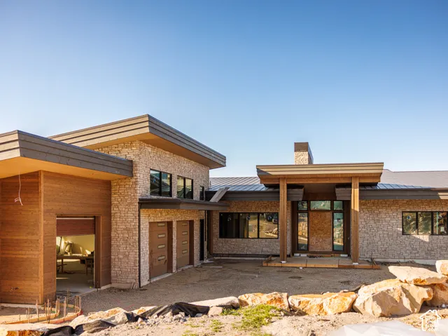 Modern exterior featuring stacked stone masonry, horizontal wood-finish siding, a metal roof, and dark-framed multi-pane windows