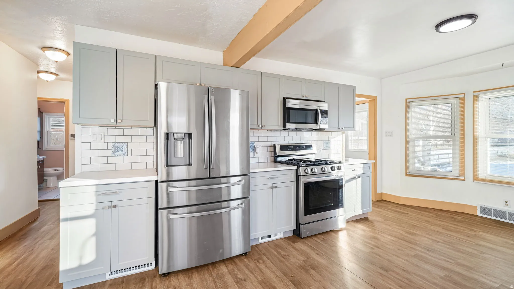 Kitchen with healthy amount of natural light, appliances with stainless steel finishes, beamed ceiling, gray cabinets, and tasteful backsplash