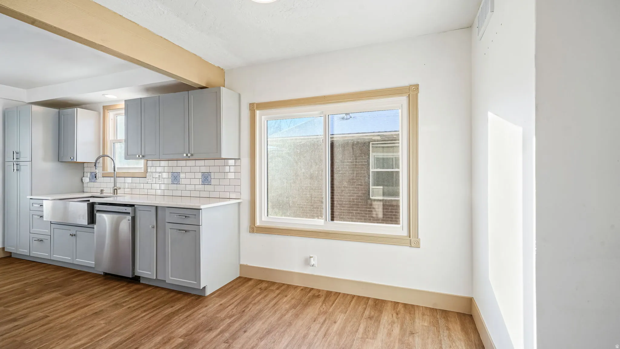 Kitchen with gray cabinets, tasteful backsplash, dishwasher, light wood finished floors, and beamed ceiling