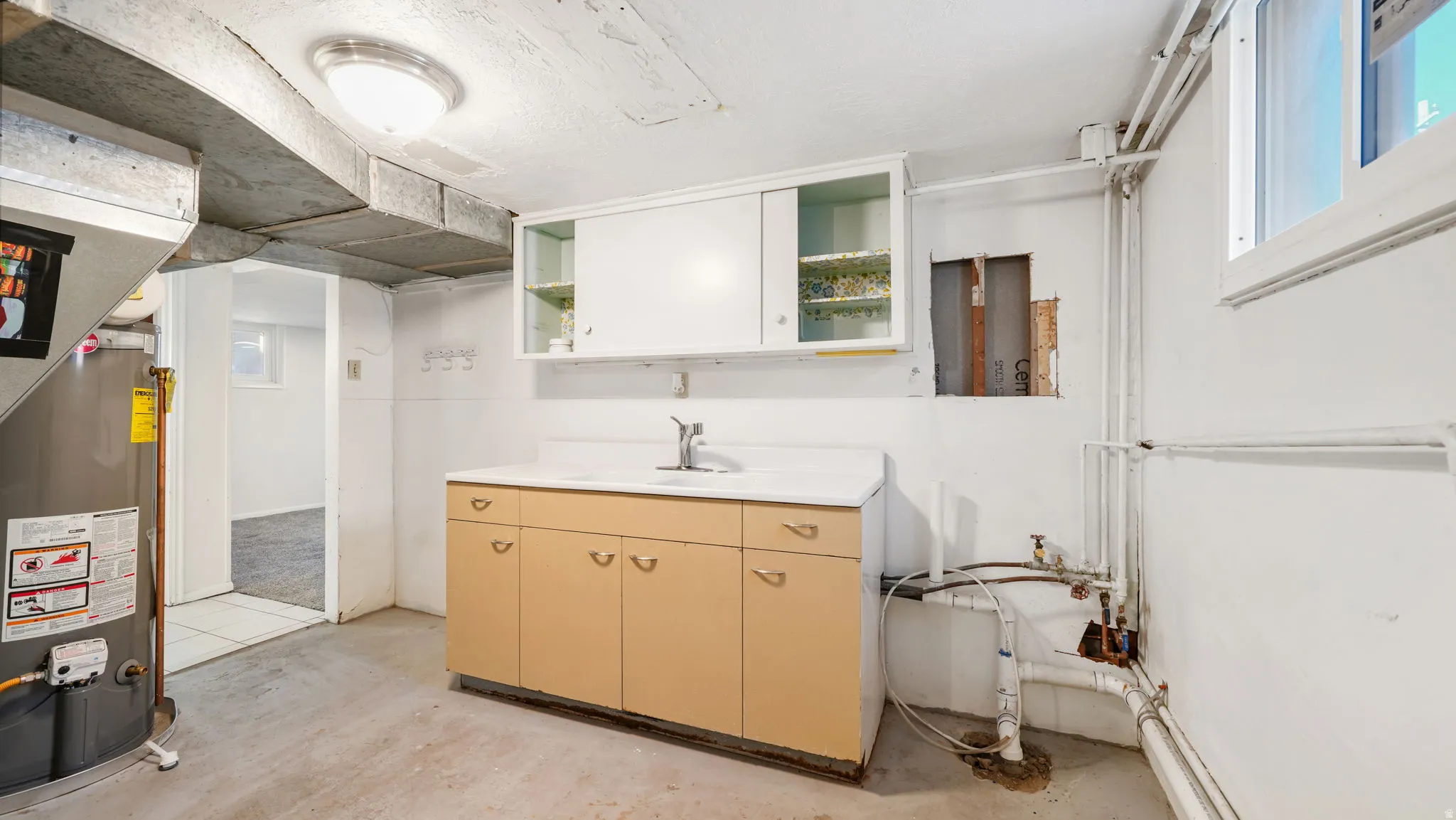 Kitchen with gas water heater, light countertops, concrete floors, and open shelves