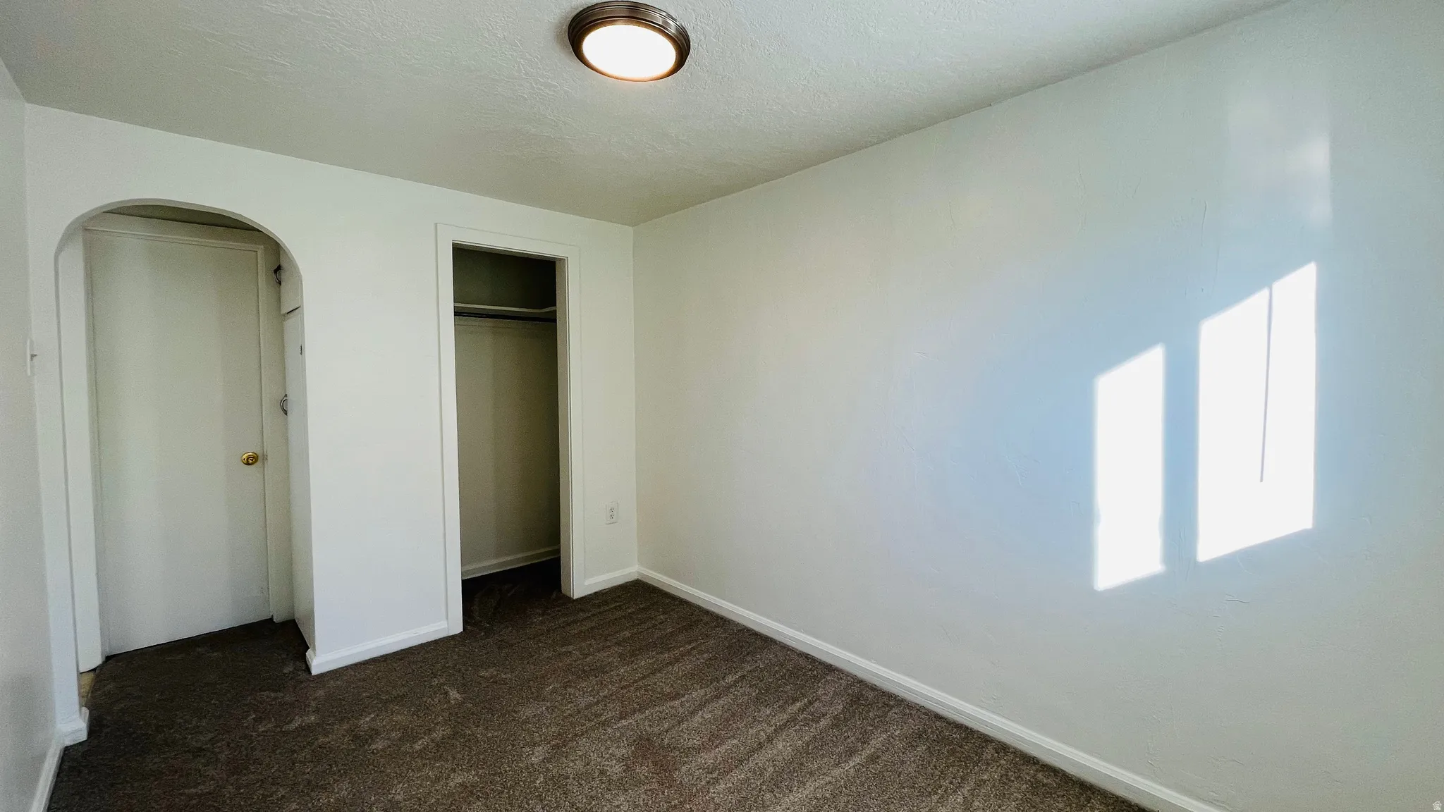 Unfurnished bedroom featuring dark carpet, a textured ceiling, a closet, and arched walkways