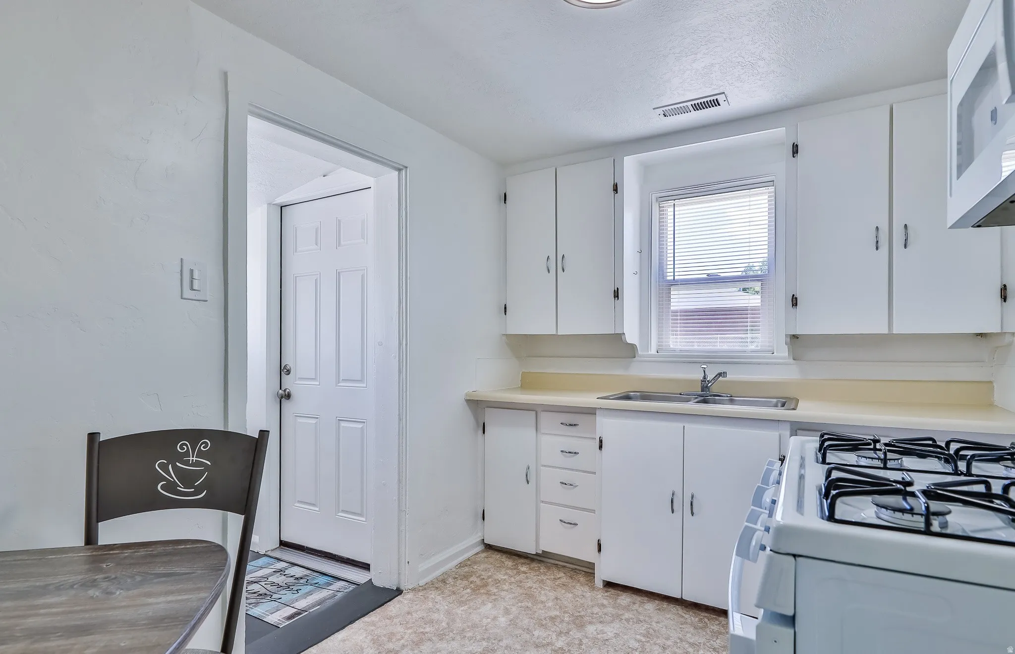 Kitchen with light countertops, white cabinets, white appliances, light floors, and a textured ceiling