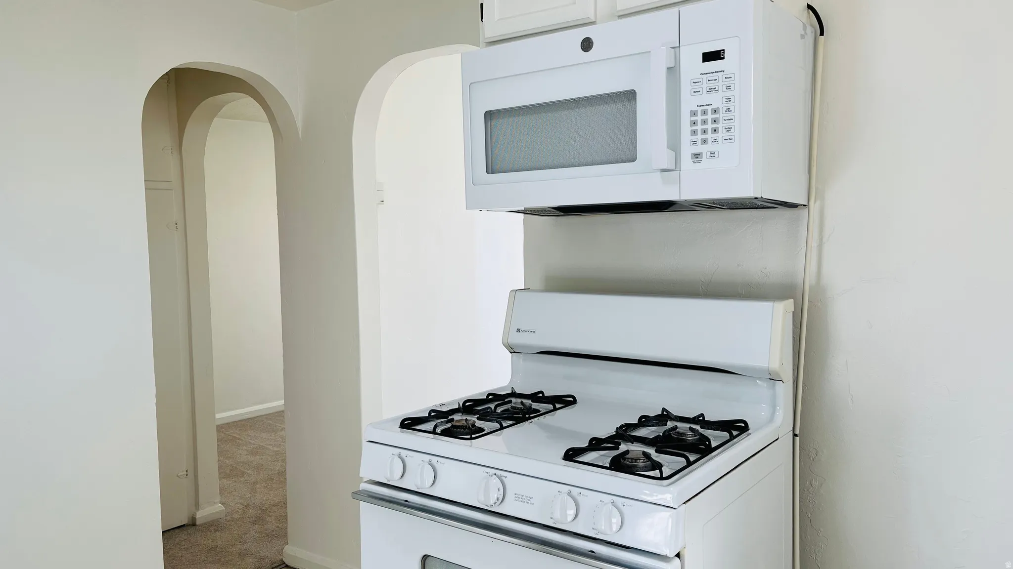 Kitchen featuring white appliances, arched walkways, and carpet
