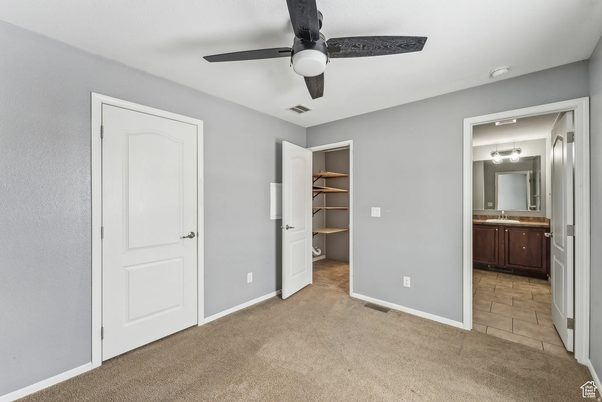 Unfurnished bedroom with a walk in closet, light carpet, ceiling fan, and connected bathroom
