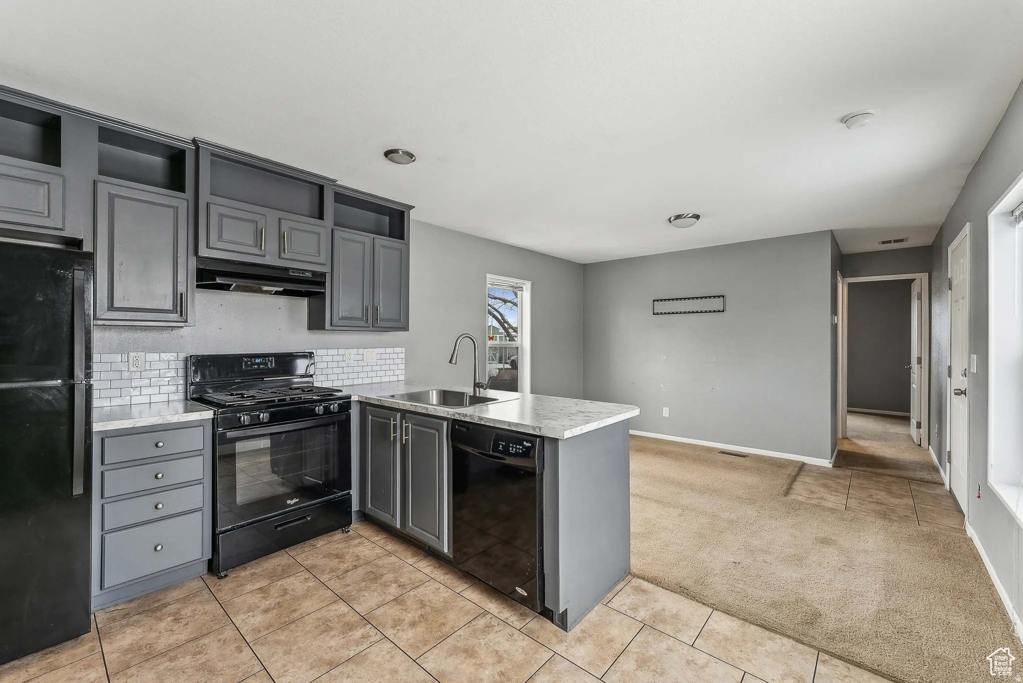 Kitchen with a peninsula, black appliances, light countertops, gray cabinets, and light colored carpet