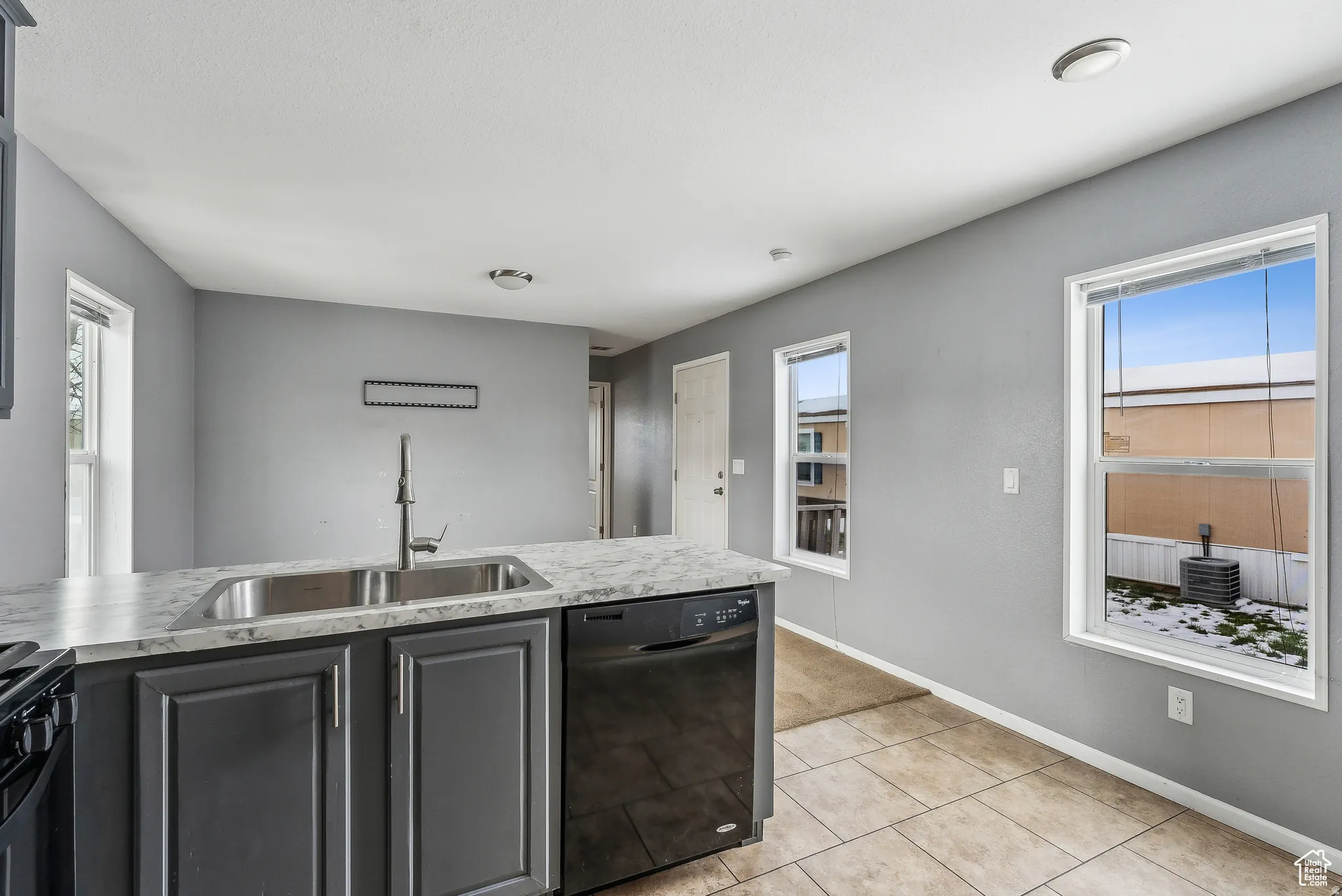 Kitchen featuring black appliances, light tile patterned floors, a peninsula, light stone counters, and gray cabinets