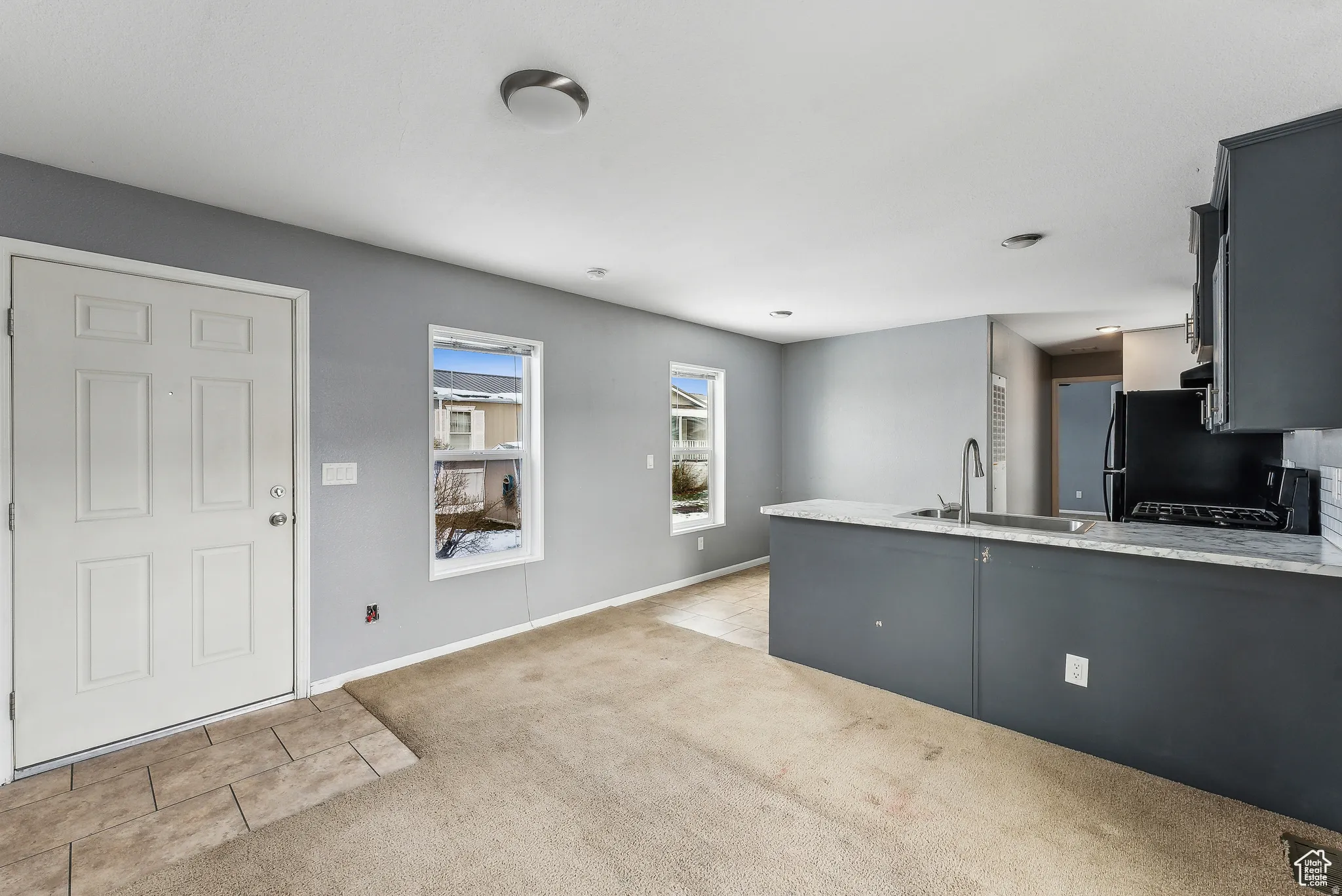 Kitchen featuring light stone counters, light colored carpet, a peninsula, black gas stove, and dark cabinets