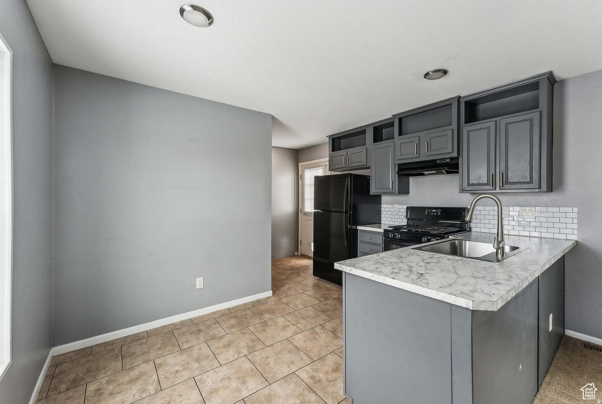Kitchen featuring gray cabinetry, black appliances, open shelves, light countertops, and decorative backsplash