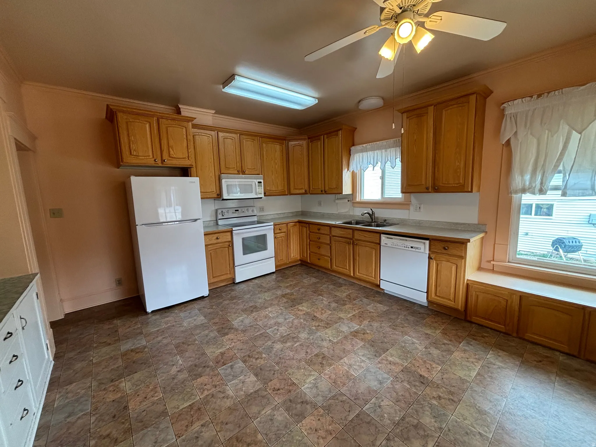 Kitchen with stone finish flooring, white appliances, ornamental molding, a ceiling fan, and light countertops