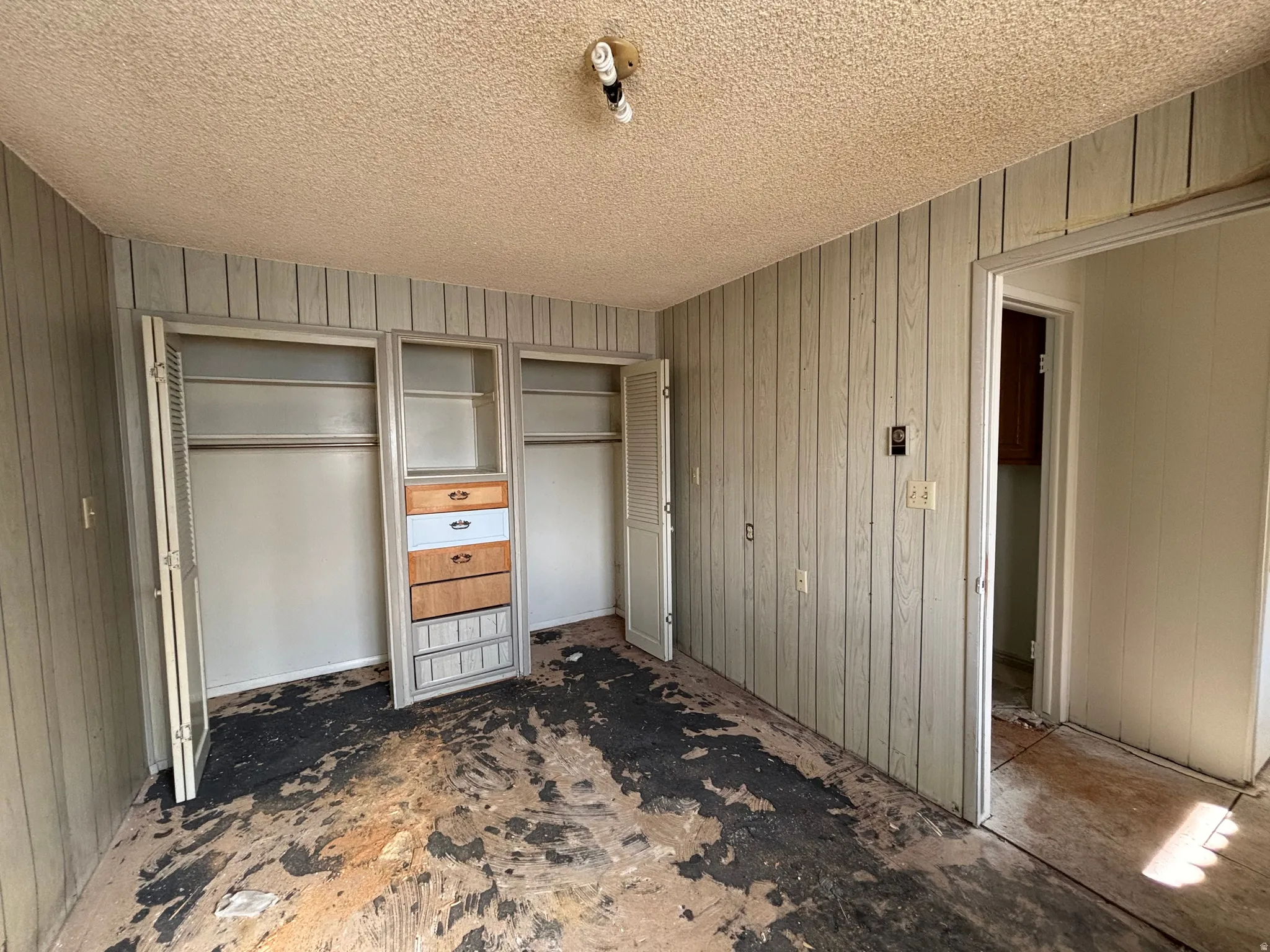 Unfurnished bedroom featuring multiple closets, a textured ceiling, and wood walls